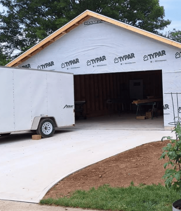 Detached garage wrapped in house wrap beside a newly poured concrete apron