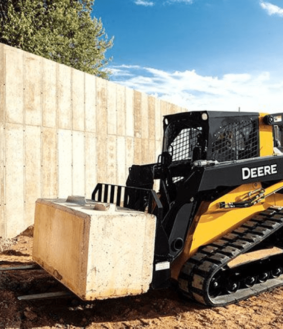 A skid-steer setting a concrete block in progress on a Hand Made Enterprises job site