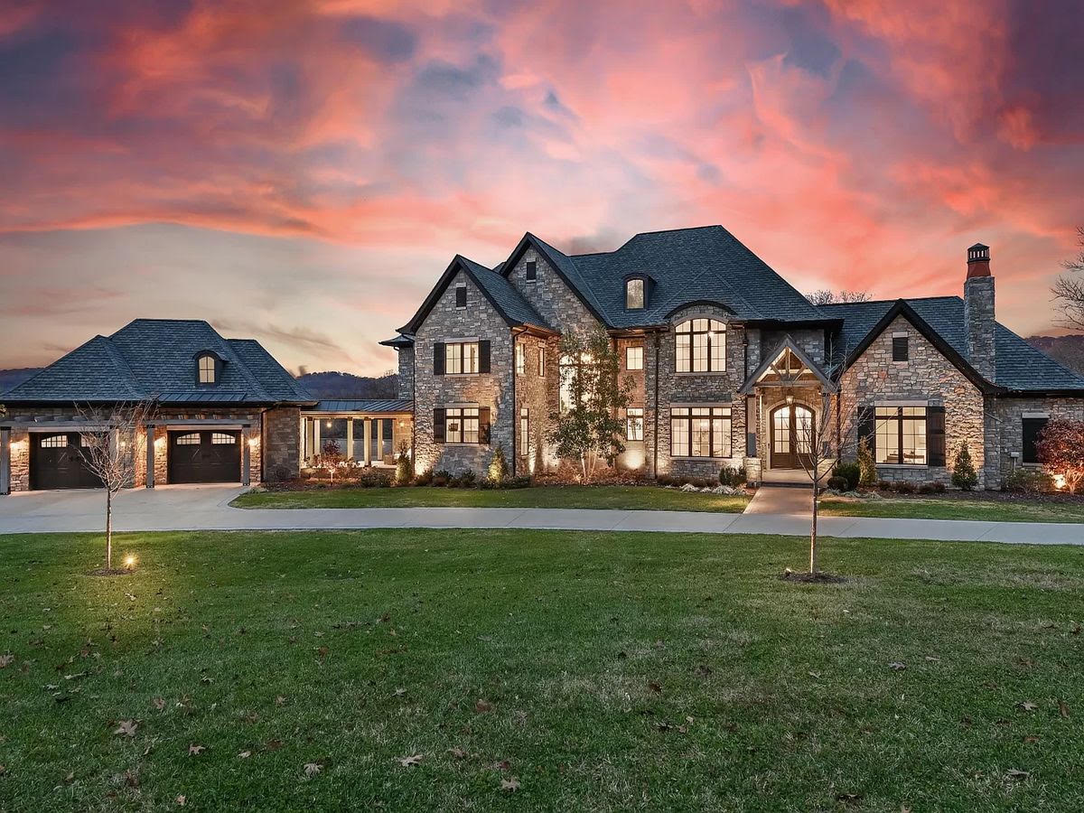 A stone estate home with a front lawn at sunset