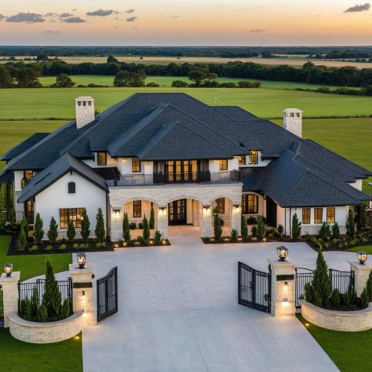 A white estate home with a gated motor court at dusk