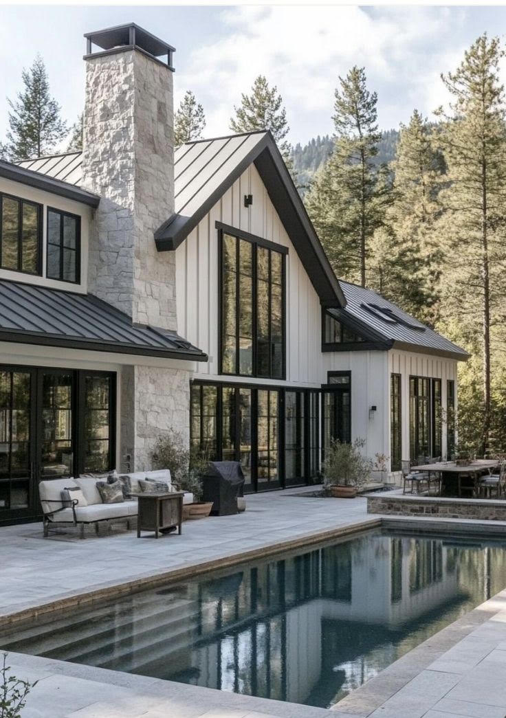 A modern farmhouse with a stone chimney, a lap pool and an outdoor living patio